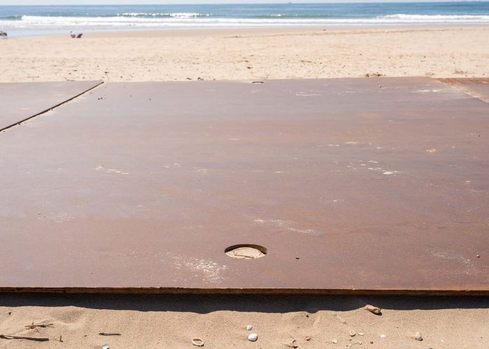 Tweedehands-stalen-rijplaten-op-strand-met-trekgat tweedehands rijplaten van staal op strand met trekgat of logo